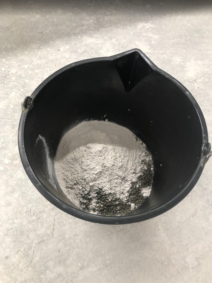 Et ftografi som viser murbøtte med gipspulver og sand som skal mikses med vann til en mørtel.