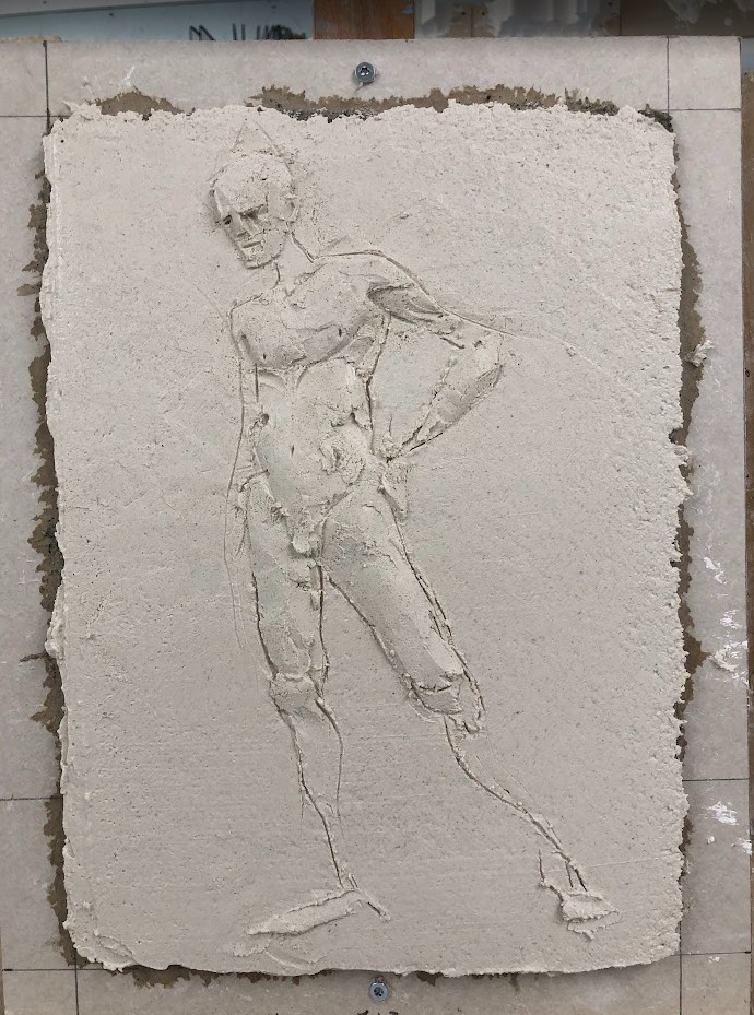 Et relieff viser en stående akt, en mann. Modellert i gipspuss på gipslate.