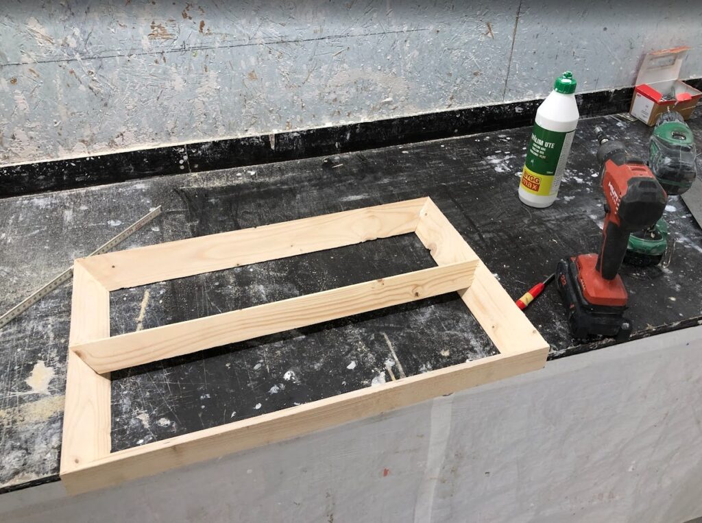 En treramme snekres sammen på verksted med skruer og lim.